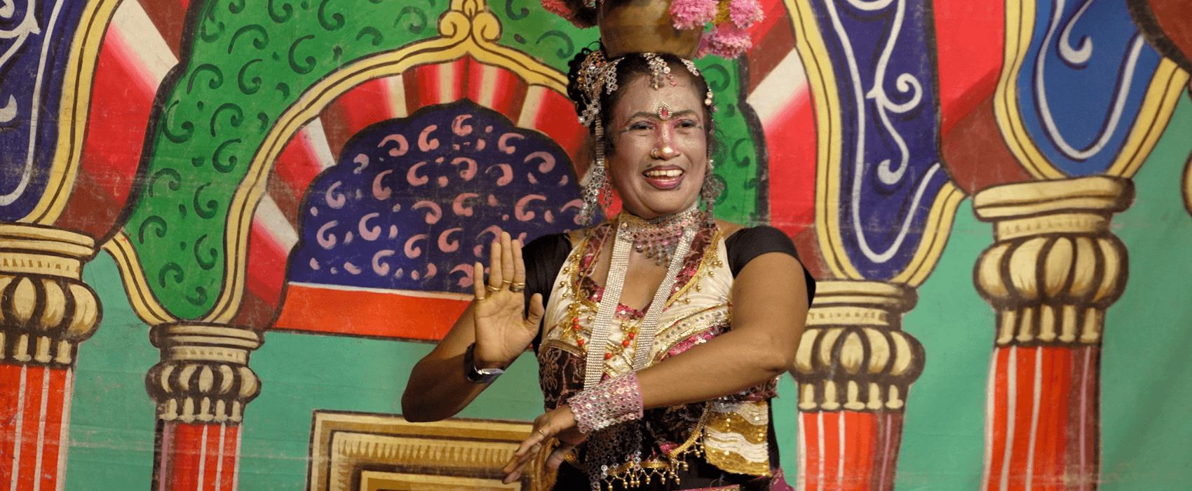 A middle-aged woman adorned with jewels and flowers commencing a dance performance, she is an erotic dancer