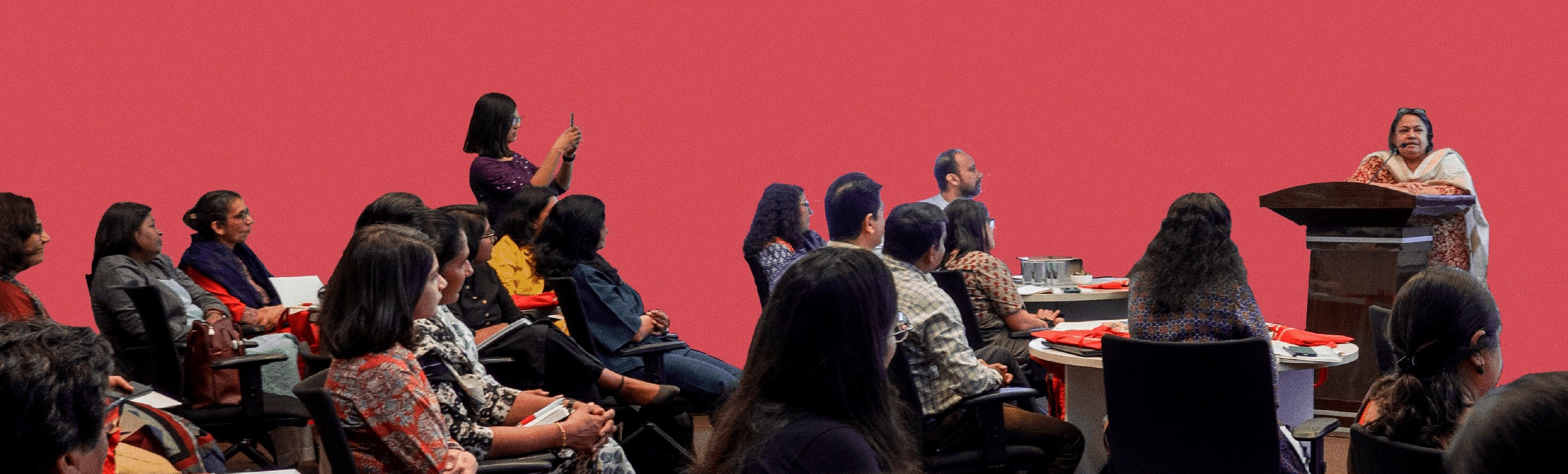 Women at a conference, one woman speaking at the podium